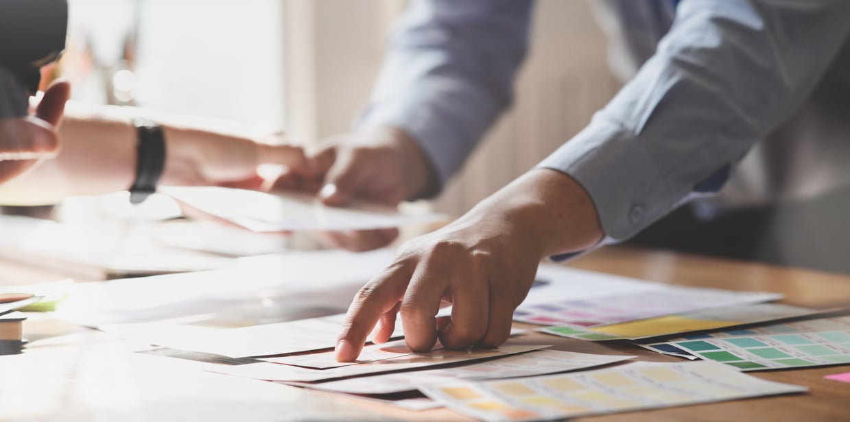 Crop coworkers interacting while standing near pile of flyers